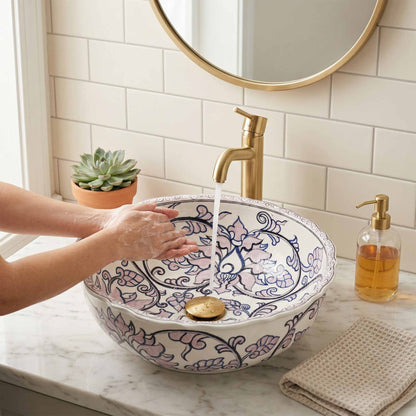 Person washing hands under a decorative sink with a gold faucet in a bathroom setting.