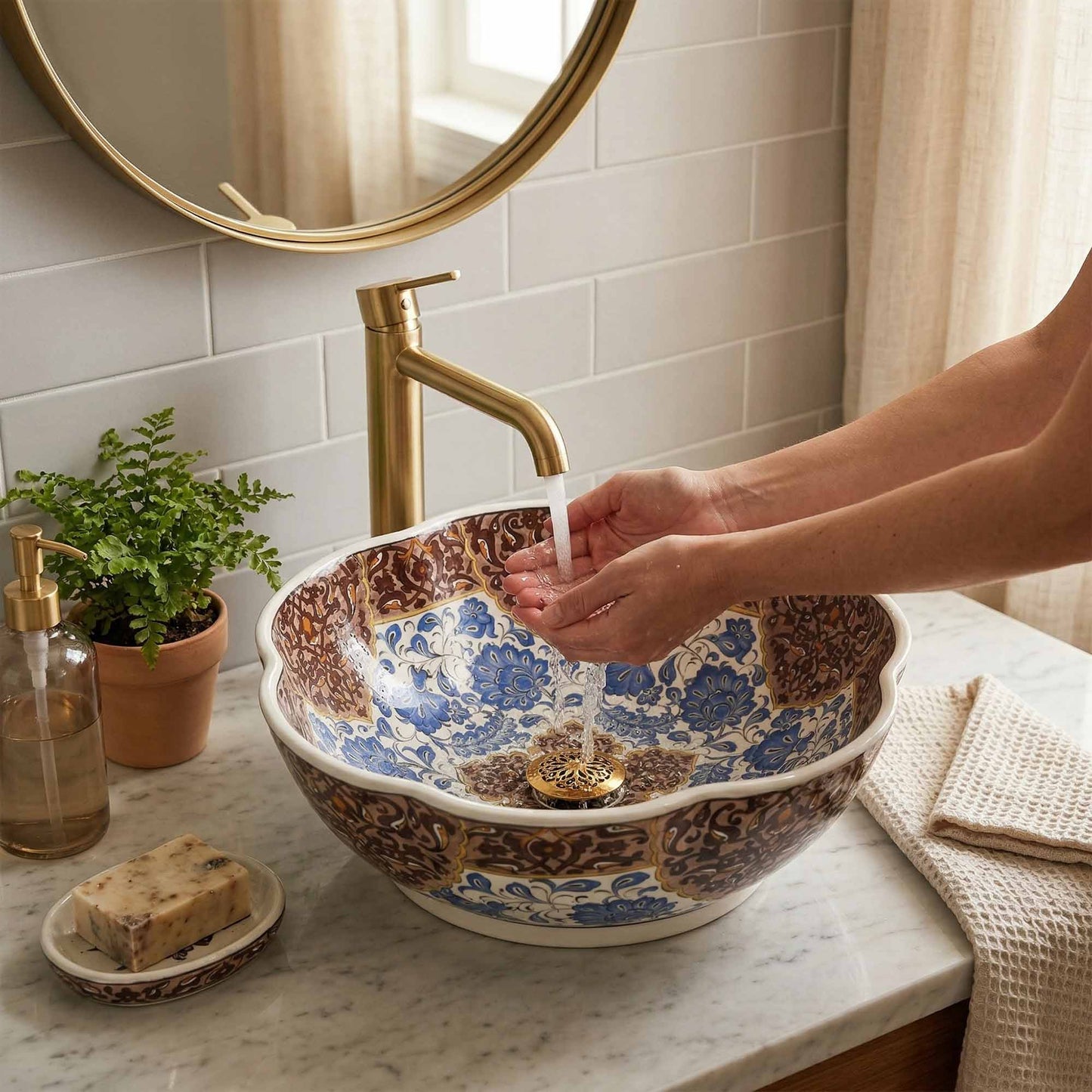 Person washing hands under a faucet in a bathroom with a decorative ceramic sink.