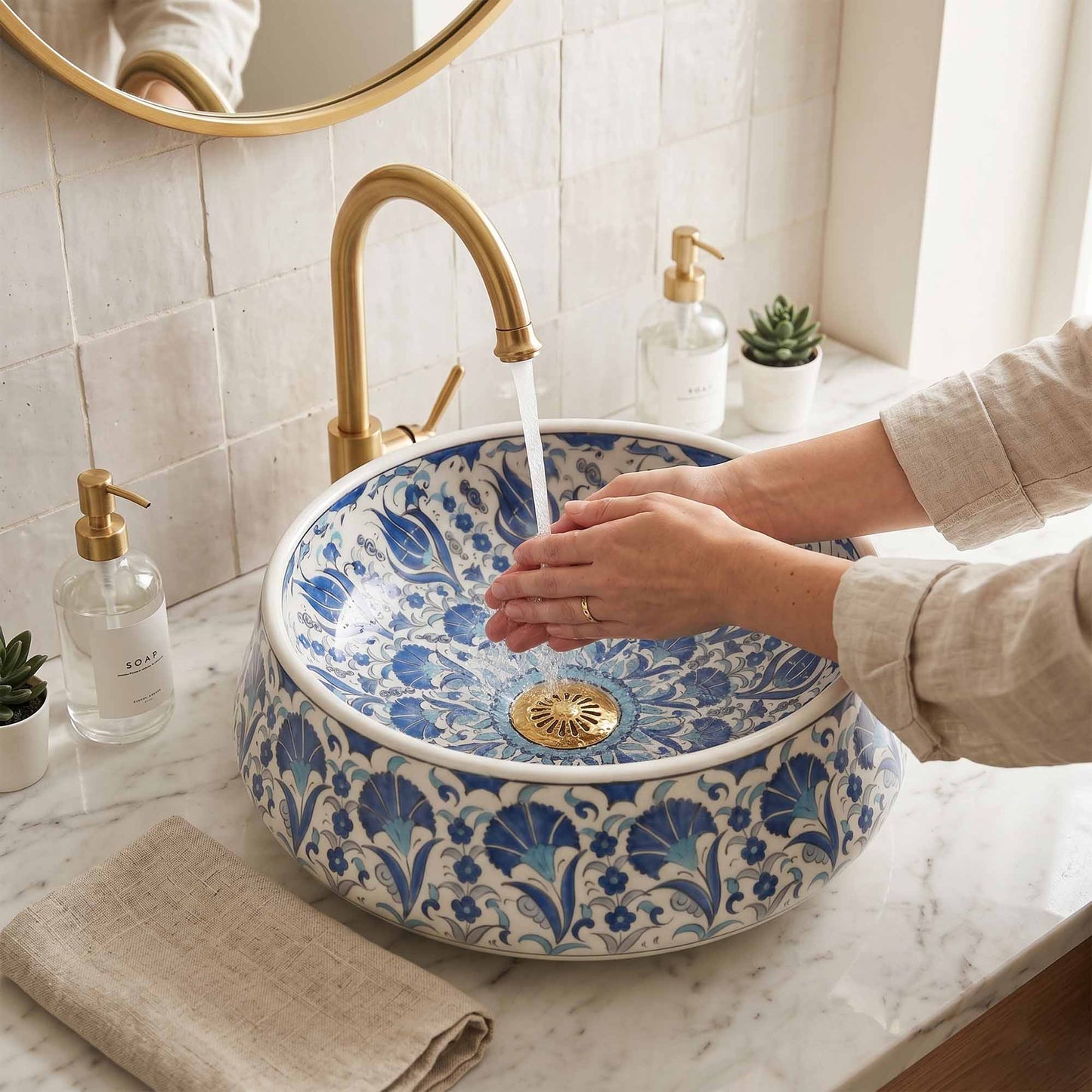 Person washing hands under a gold faucet in a bathroom with a decorative blue and white sink.