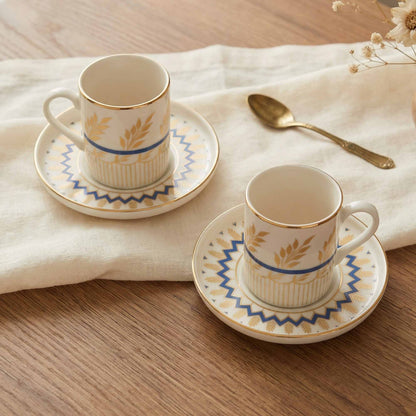Two porcelain coffee cups with saucers on a wooden table with a white cloth.